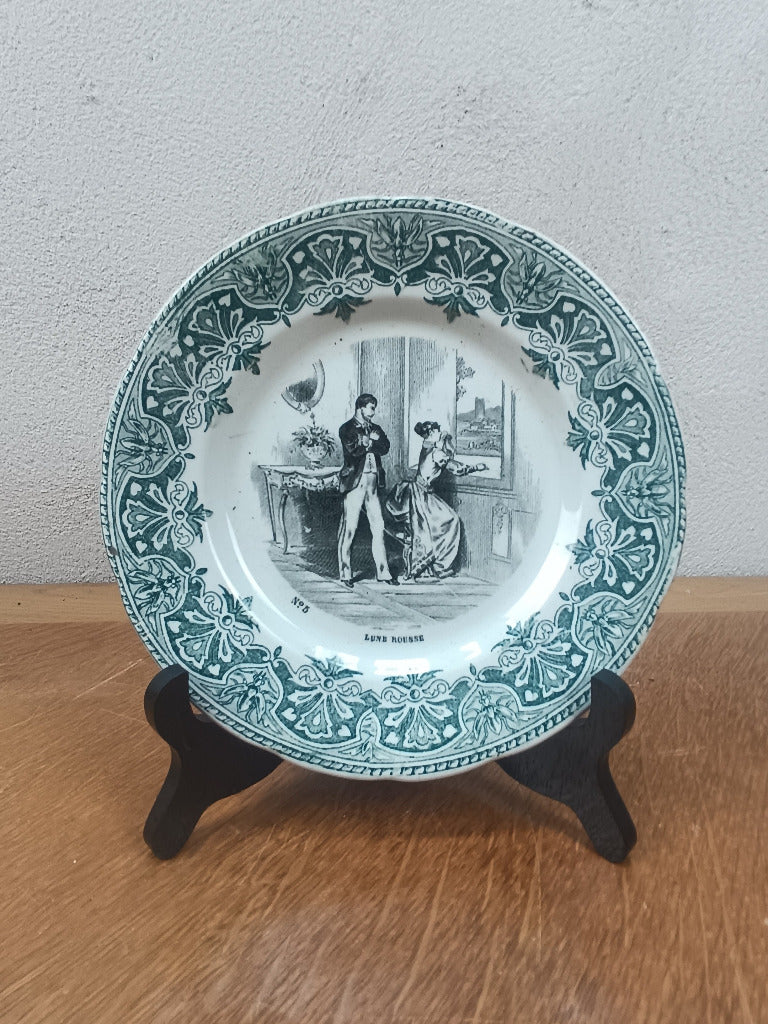 Assiette parlante Creil et Montereau « Lune rousse » numéro 3, représentant un couple et ornée d’une bordure vert foncé, diamètre 19 cm.