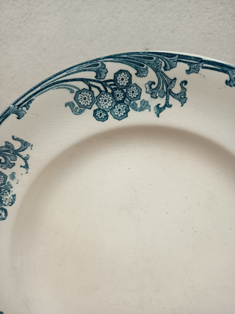Assiette ancienne Longwy Les Églantines en terre de fer, décor floral bleu-vert sur fond ivoire, diamètre 23,5 cm.