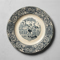 Assiette Gien L’Hercule n° 12 à scène foraine et bordure végétale noire sur fond ivoire