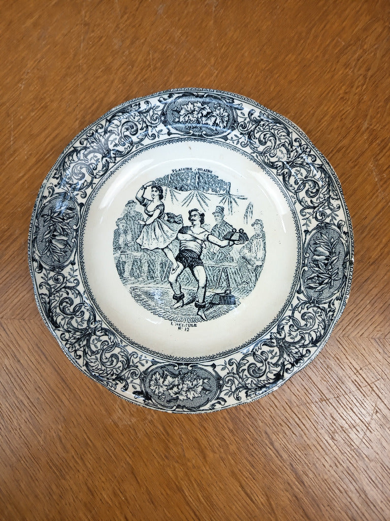 Assiette Gien L’Hercule n° 12 à scène foraine et bordure végétale noire sur fond ivoire