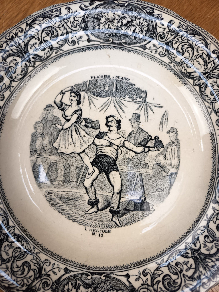 Assiette Gien L’Hercule n° 12 à scène foraine et bordure végétale noire sur fond ivoire